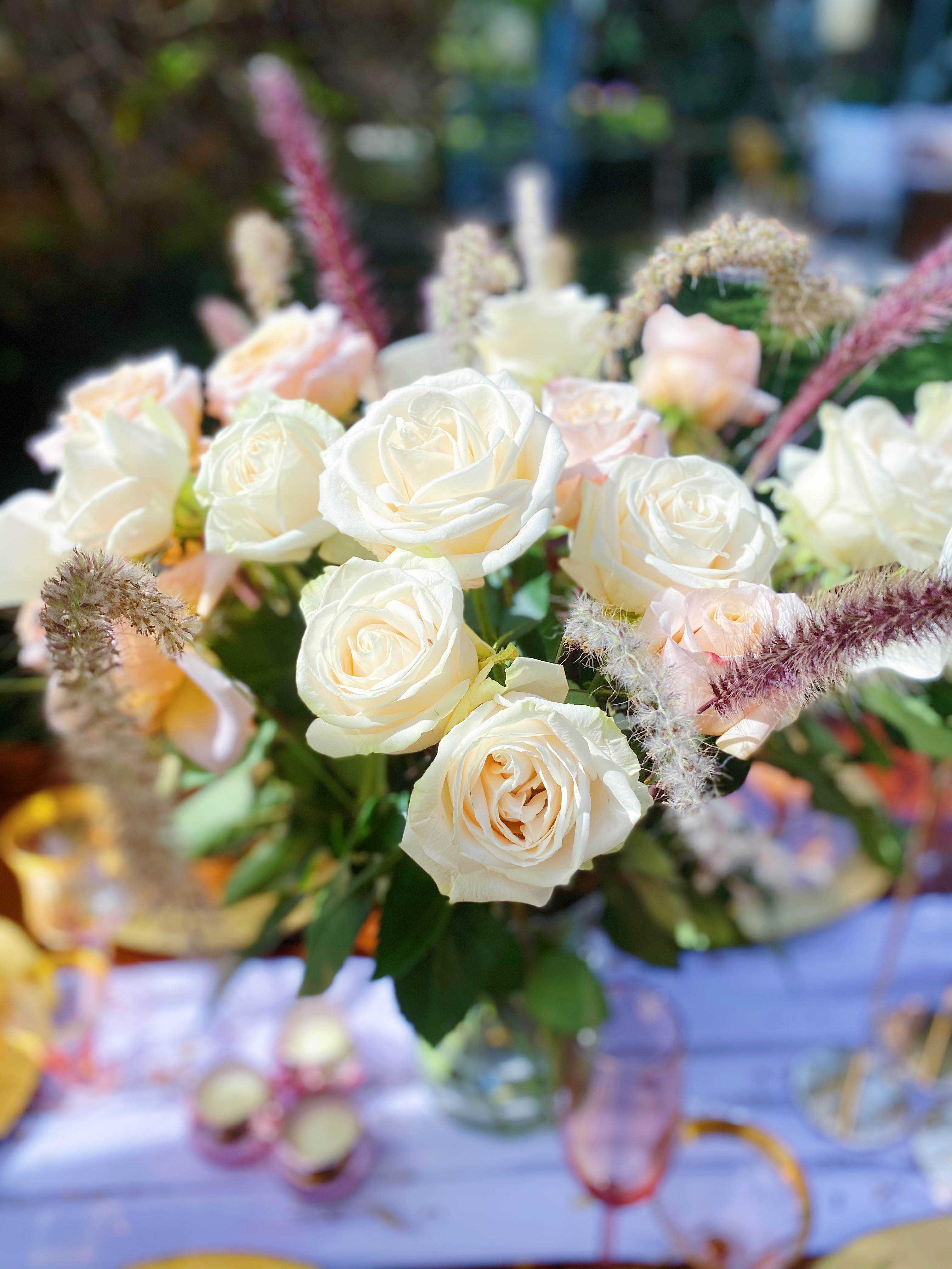 White roses in a vase in focus, with candles and pink champagne glasses in the background